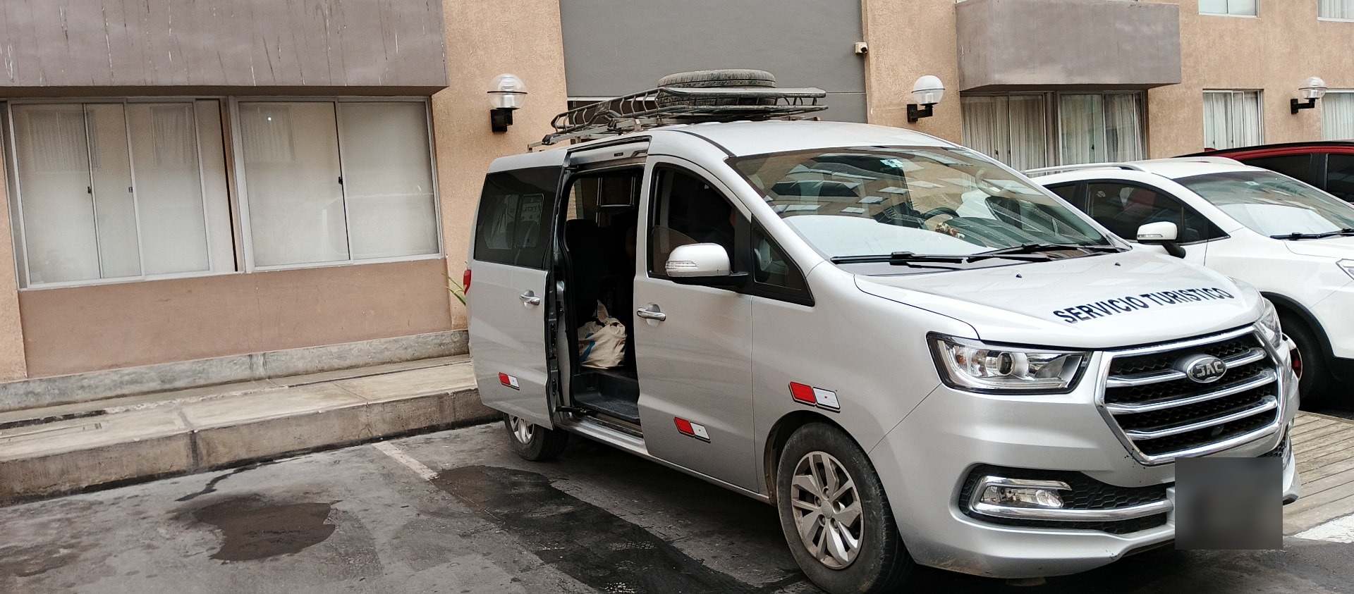 Van JAC M4 con puerta lateral abierta y parrilla de techo cargada